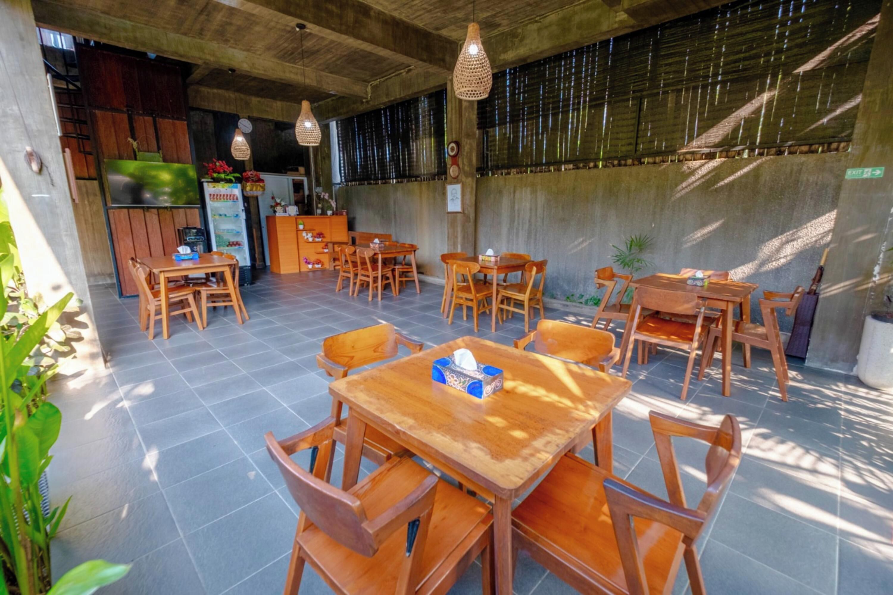 Un restaurante con mesas y sillas de madera, un refrigerador y luces colgantes.