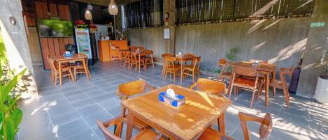 Un restaurante con mesas y sillas de madera, un refrigerador y luces colgantes.