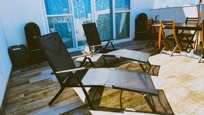 Une terrasse extérieure avec une table et des chaises, un grand parasol et une vue sur le ciel à travers des fenêtres à motifs.