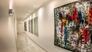 Un couloir avec une grande peinture abstraite sur le mur de droite, un sol en marbre et un éclairage encastré.