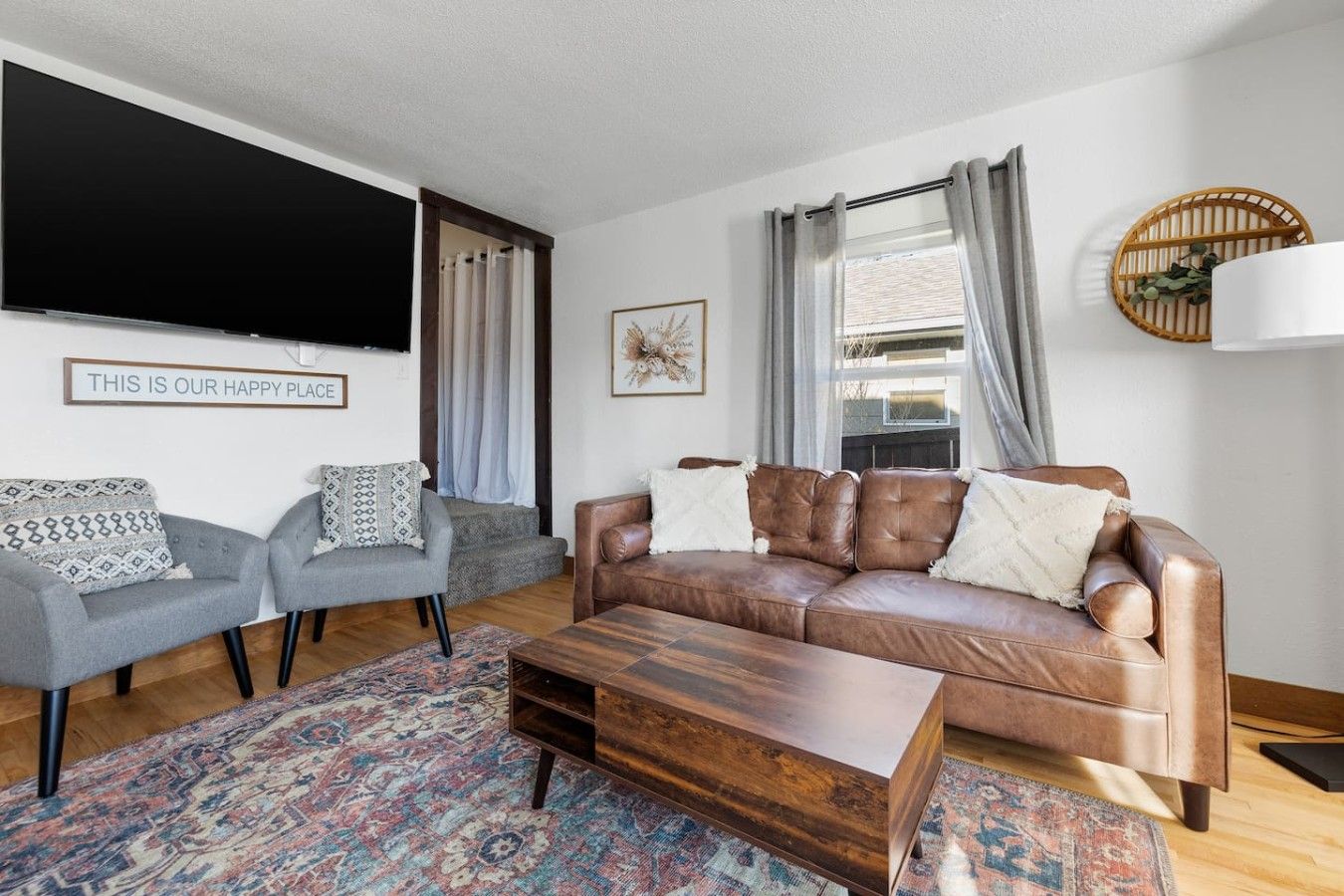 A living room with a sofa, two armchairs, a coffee table, a flat-screen TV, and a decorative wall piece.