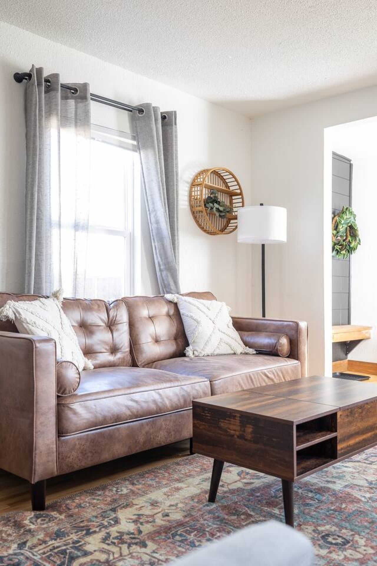 A brown leather sofa with cushions, a wooden coffee table, a patterned rug, a wall-mounted lamp, and a decorative wall piece.