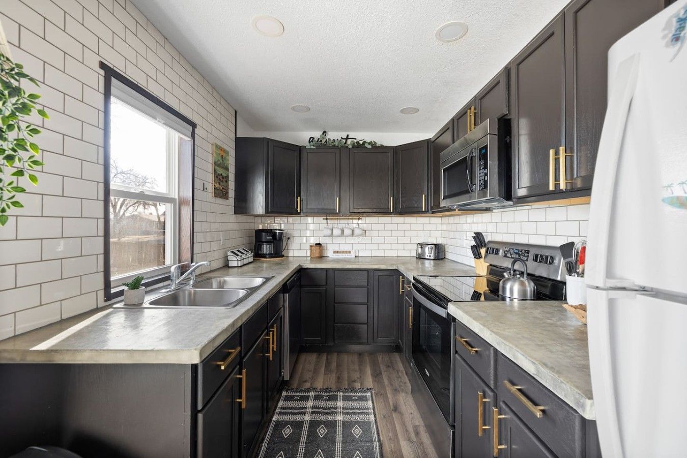 A modern kitchen with dark cabinetry, stainless steel appliances, and a large window providing natural light.