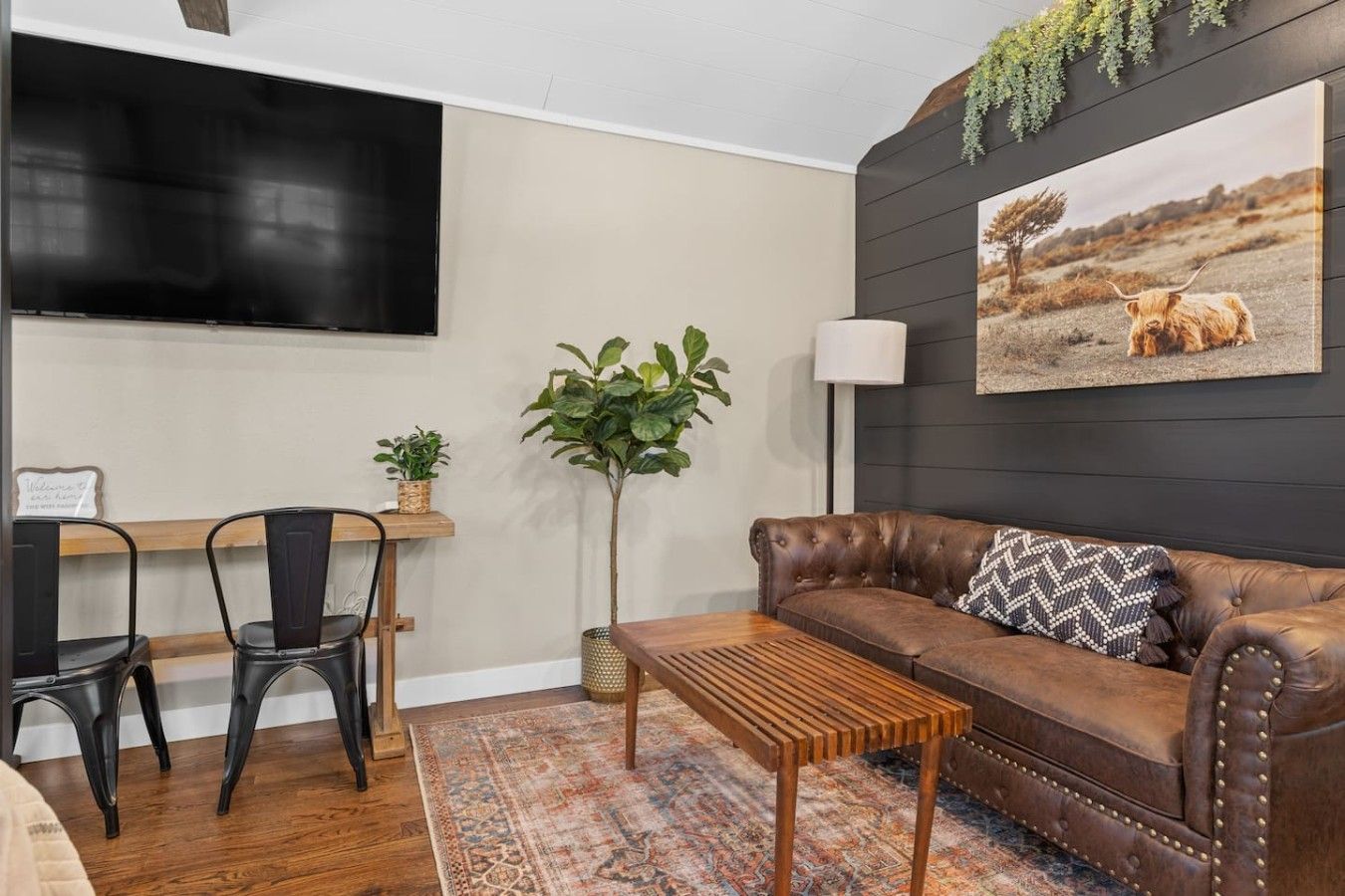 Una sala de estar con un sofá de cuero, una mesa de centro de madera, un televisor montado en la pared y una planta.