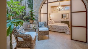 A cozy room with a bed, a chair, a small table, and a large window with a view of greenery. - Elegant Ground Floor Apartment in Historic Centre (ST REMY DE PROVENCE)