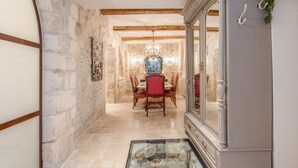 A stone-walled hallway leading to a dining area with a chandelier, wooden chairs, and a glass table. - Elegant Ground Floor Apartment in Historic Centre (ST REMY DE PROVENCE)