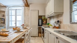 A kitchen with a wooden table, white cabinets, a sink, and a window with curtains. - Elegant Ground Floor Apartment in Historic Centre (ST REMY DE PROVENCE)