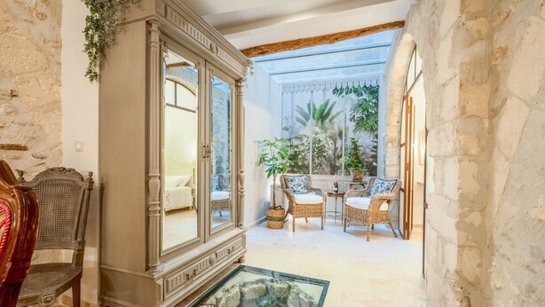 A room with a large armoire, a glass table with a rock display, wicker furniture, and a view of a balcony with plants. - Elegant Ground Floor Apartment in Historic Centre (ST REMY DE PROVENCE)