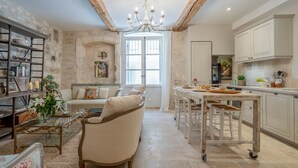 A spacious living area with a sofa, a glass coffee table, and a bookshelf. There is a kitchen area with a dining table and chairs. - Elegant Ground Floor Apartment in Historic Centre (ST REMY DE PROVENCE)