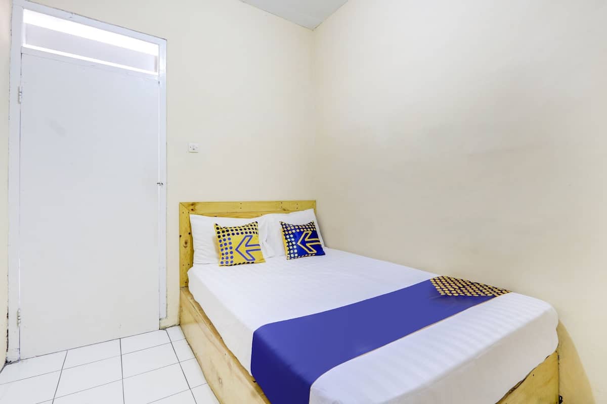 Ein kleines, sauberes Zimmer mit einem Einzelbett, einem hölzernen Kopfteil und einer weißen Tür.