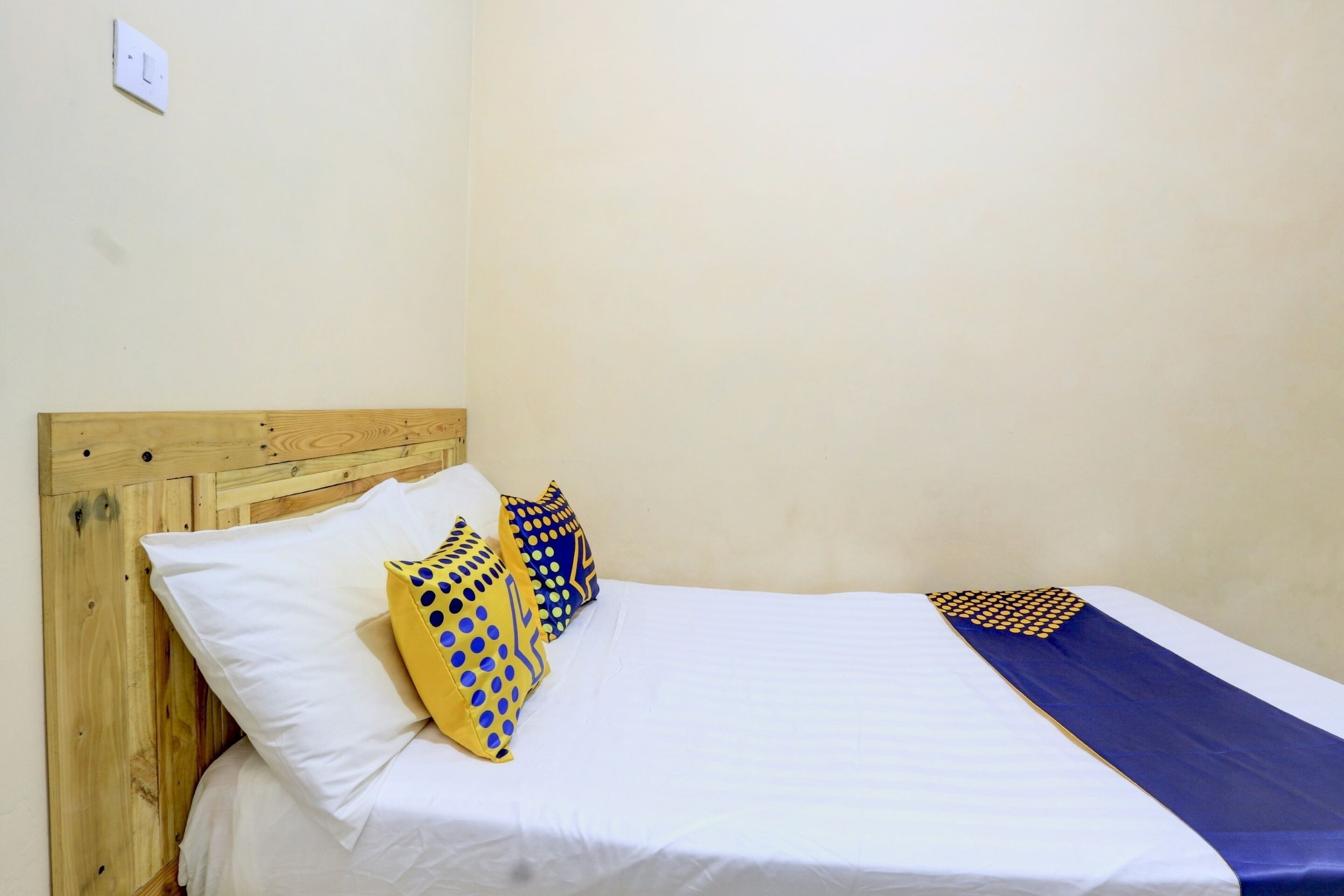 Una cama individual con ropa blanca, cabecera de madera y dos almohadas decorativas.