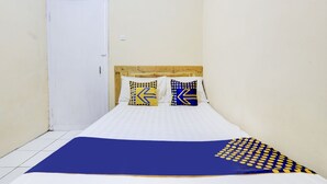 Une petite pièce étroite, avec un lit simple, du linge de lit blanc et deux oreillers aux motifs géométriques.