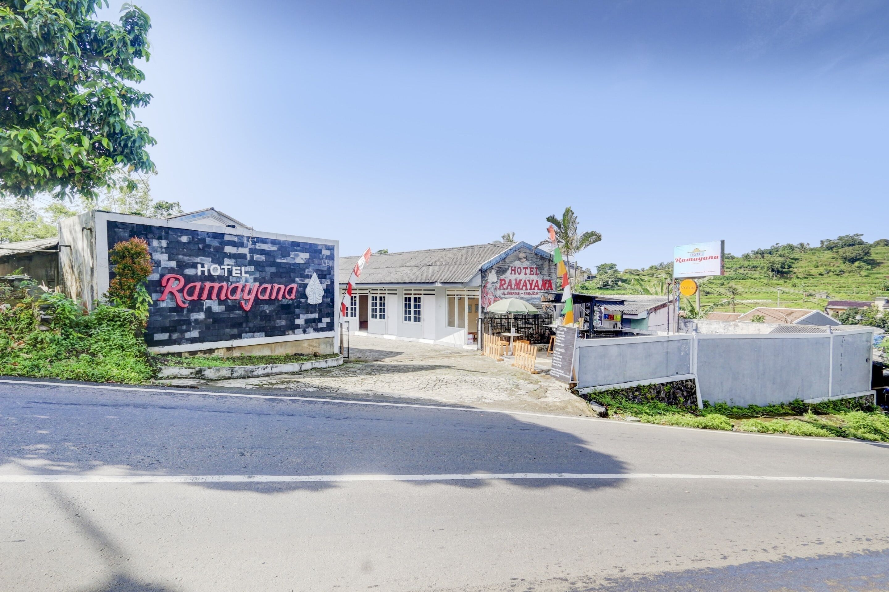 A hotel named Ramayana with a prominent sign, a small building with a sloped roof, and a signboard for Ramayana.