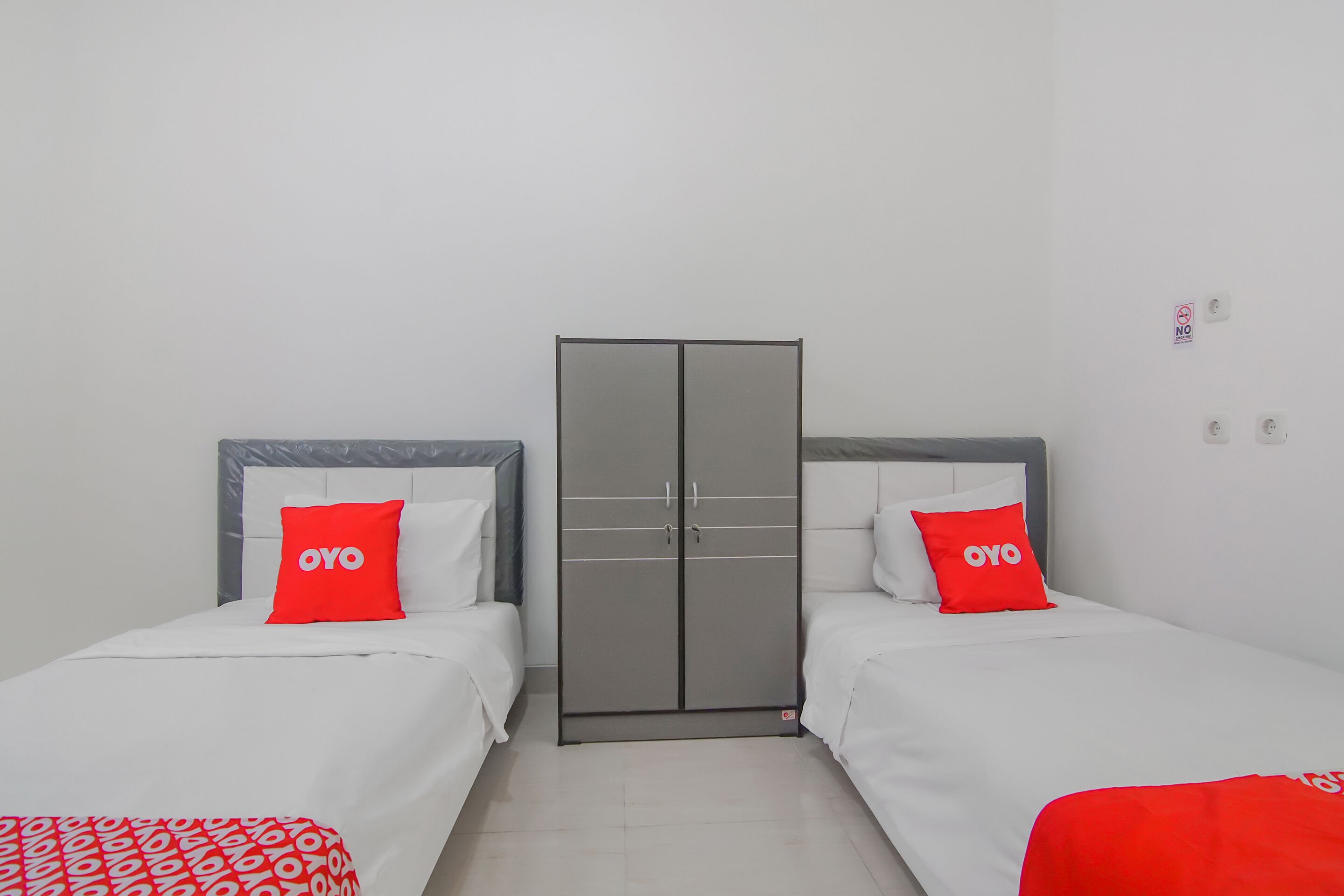 Een hotelkamer met twee bedden, een kledingkast en een bordje 'ROKEN VERBODEN' aan de muur.