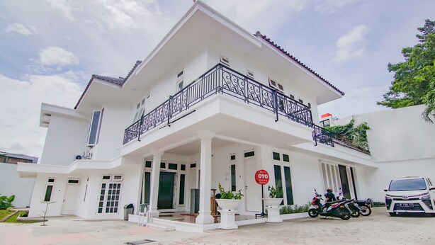 A white two-story building with a balcony, a stop sign, and two motorcycles parked in front. - Capital O 90342 Kemang Garden (Jakarta)