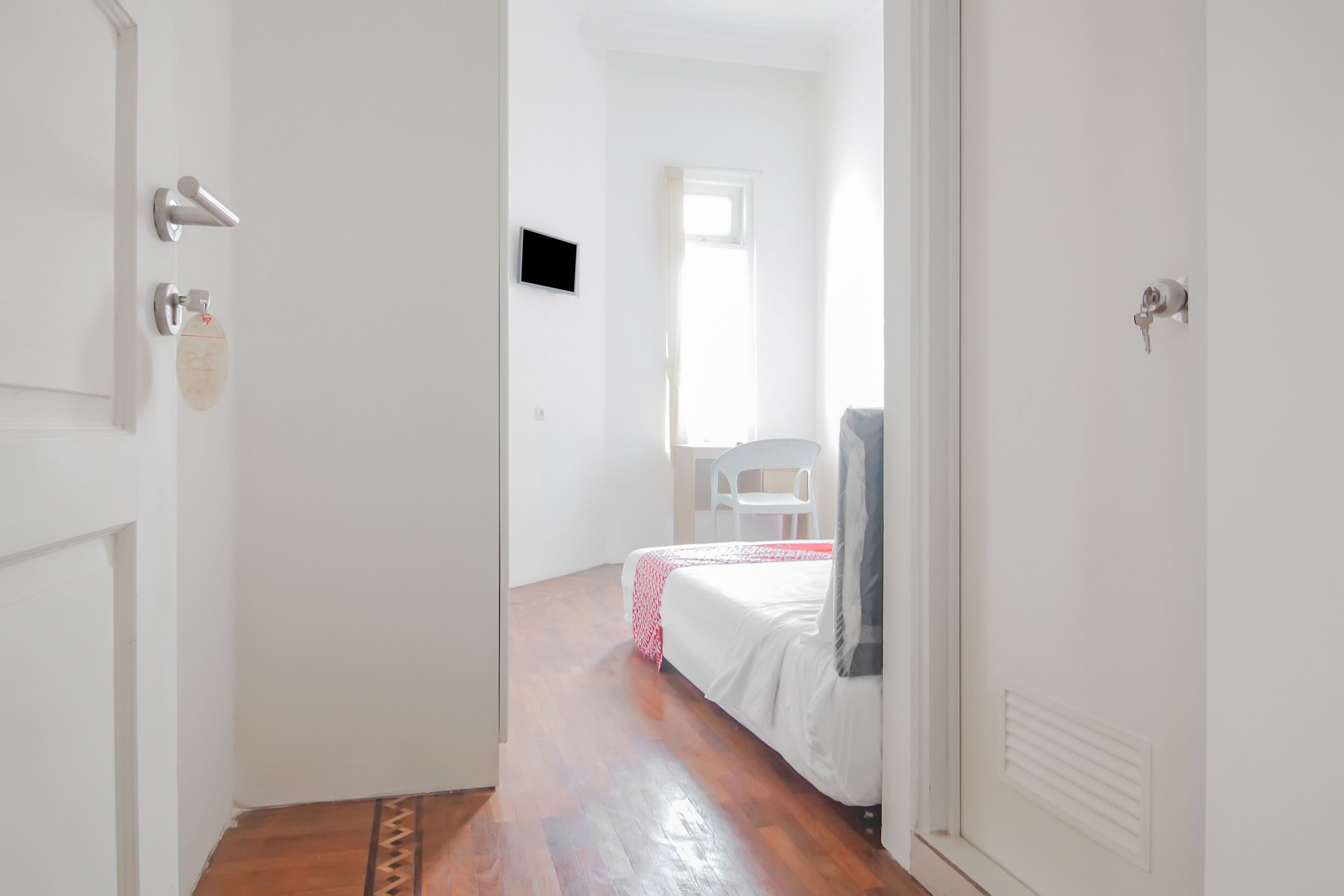 Un pasillo estrecho que conduce a un dormitorio con una cama, una silla y un televisor.