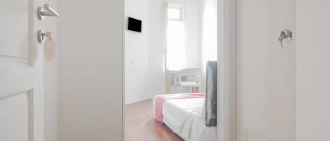 Ein schmaler Flur führt zu einem Schlafzimmer mit einem Bett, einem Sessel und einem Fernseher.