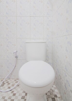 A bathroom with a toilet, a shower hose, and patterned tiles on the walls and floor. - Capital O 90342 Kemang Garden (Jakarta)