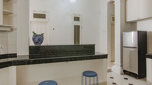 A kitchen with white cabinets, a black countertop, a blue vase, and a stainless steel refrigerator. - Capital O 90342 Kemang Garden (Jakarta)