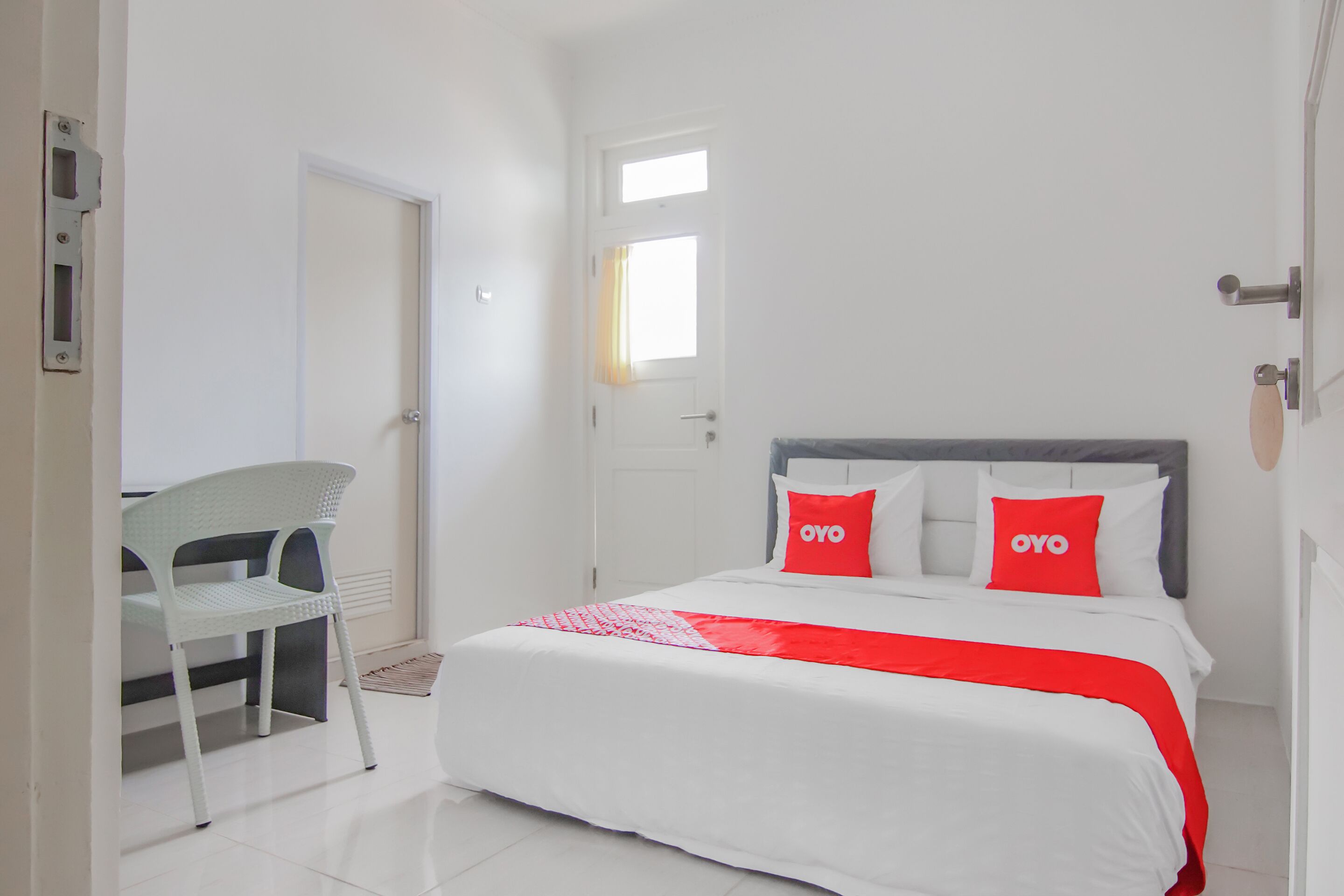 A hotel room with a bed, a chair, a window, and a door.