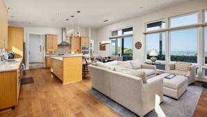 A spacious living area with a large sofa and a dining table, a kitchen with wooden cabinets, and large windows offering a view of the landscape. - Magnificent Panoramic Valley and Vineyard Views, Single Level Two Guest Suite Layout, Amazing Deck (Dundee)