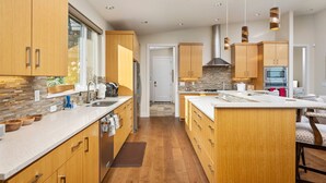 A modern kitchen with wooden cabinets, a large island, and a stone backsplash. - Magnificent Panoramic Valley and Vineyard Views, Single Level Two Guest Suite Layout, Amazing Deck (Dundee)