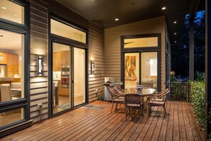 A modern house with a wooden deck, a dining area with wicker chairs, and a kitchen visible through glass doors. - Magnificent Panoramic Valley and Vineyard Views, Single Level Two Guest Suite Layout, Amazing Deck (Dundee)