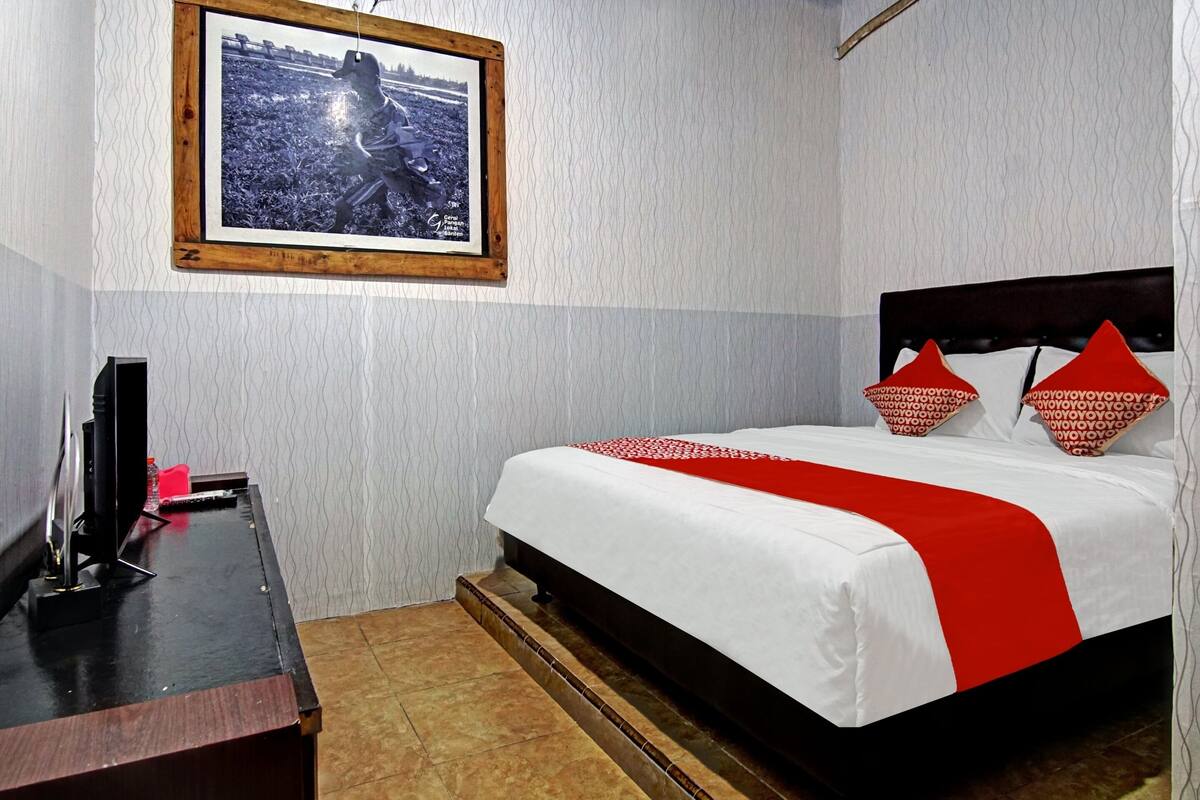 Una habitación de hotel con cama, escritorio, televisor y un cuadro en la pared.