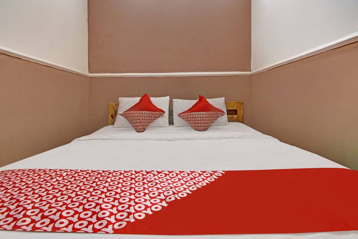 Una habitación de hotel con una cama, dos almohadas de estampado rojo y blanco, y una manta rojo y blanco.