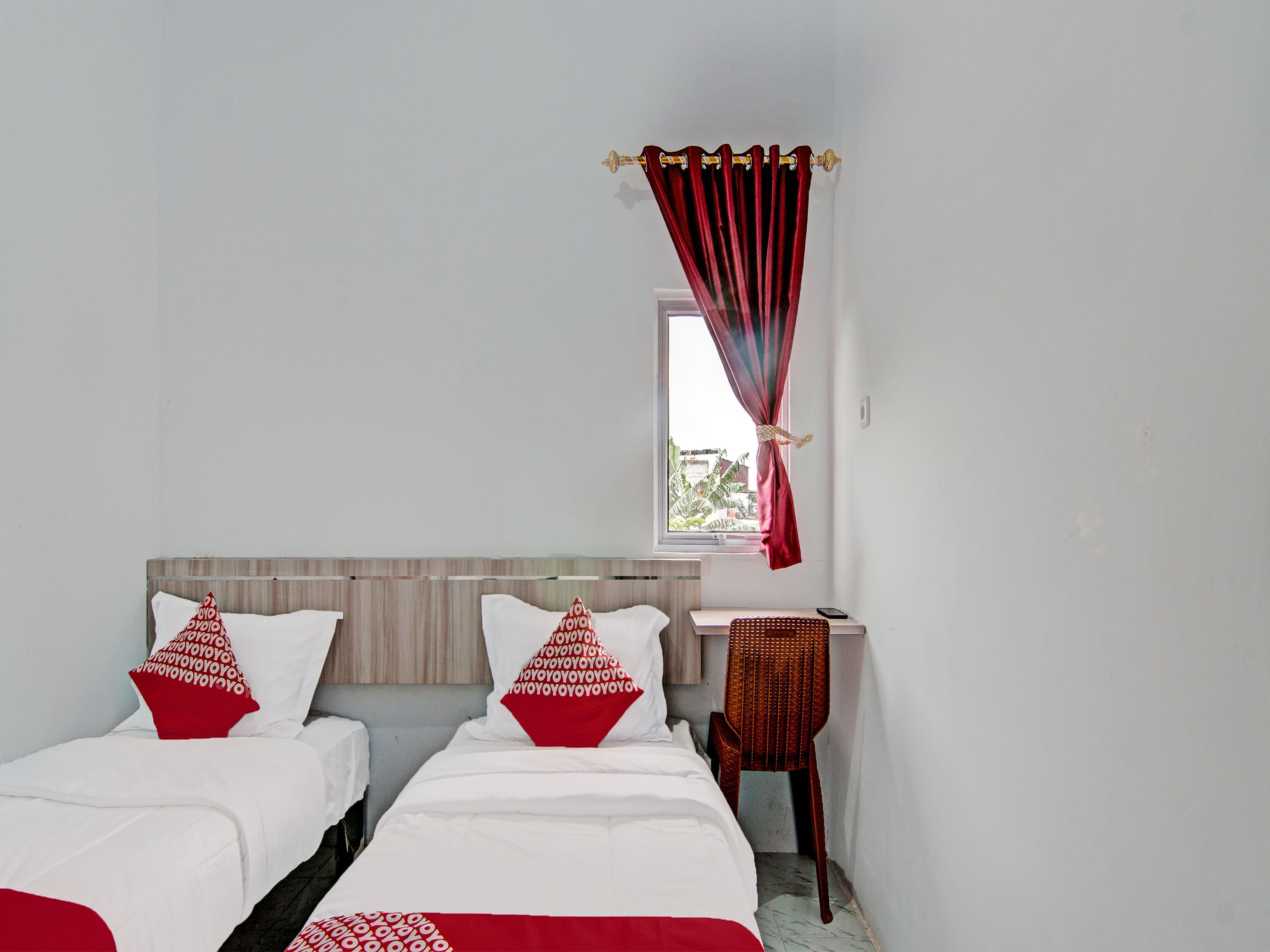 A bedroom with two beds, a small window, and a chair.