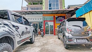 A building with a green and brown facade, a visible shop with a red door, and two parked vehicles. - OYO 92047 Penginapan Arfi Syariah (Pekanbaru)