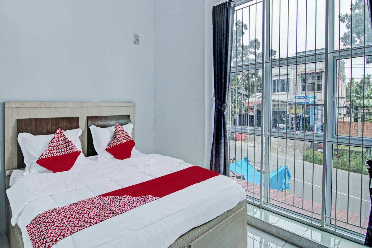 Una cama con cabecera de madera, ropa de cama blanca y almohadas con estampado rojo y blanco.