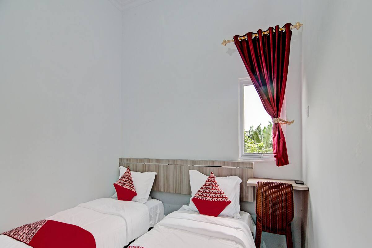Una habitación con dos camas, una mesita de noche y una ventana con cortinas rojas.