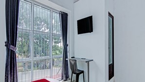 A hotel room with a large window, a desk with a chair, a bed with a red and white bedspread, and a flat-screen TV mounted on the wall. - OYO 92047 Penginapan Arfi Syariah (Pekanbaru)