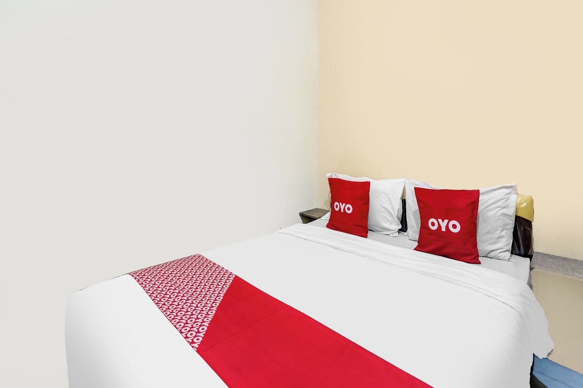 Un lit recouvert d’une couvre-lit blanche et rouge, deux oreillers ornés du mot « OYO », et une petite table de chevet avec un téléphone.