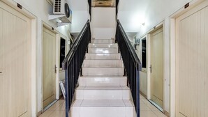 A clean, well-lit hallway with a marble staircase, wooden doors, and a black railing. - OYO 91361 Benlin D'kost Syariah (Surabaya)