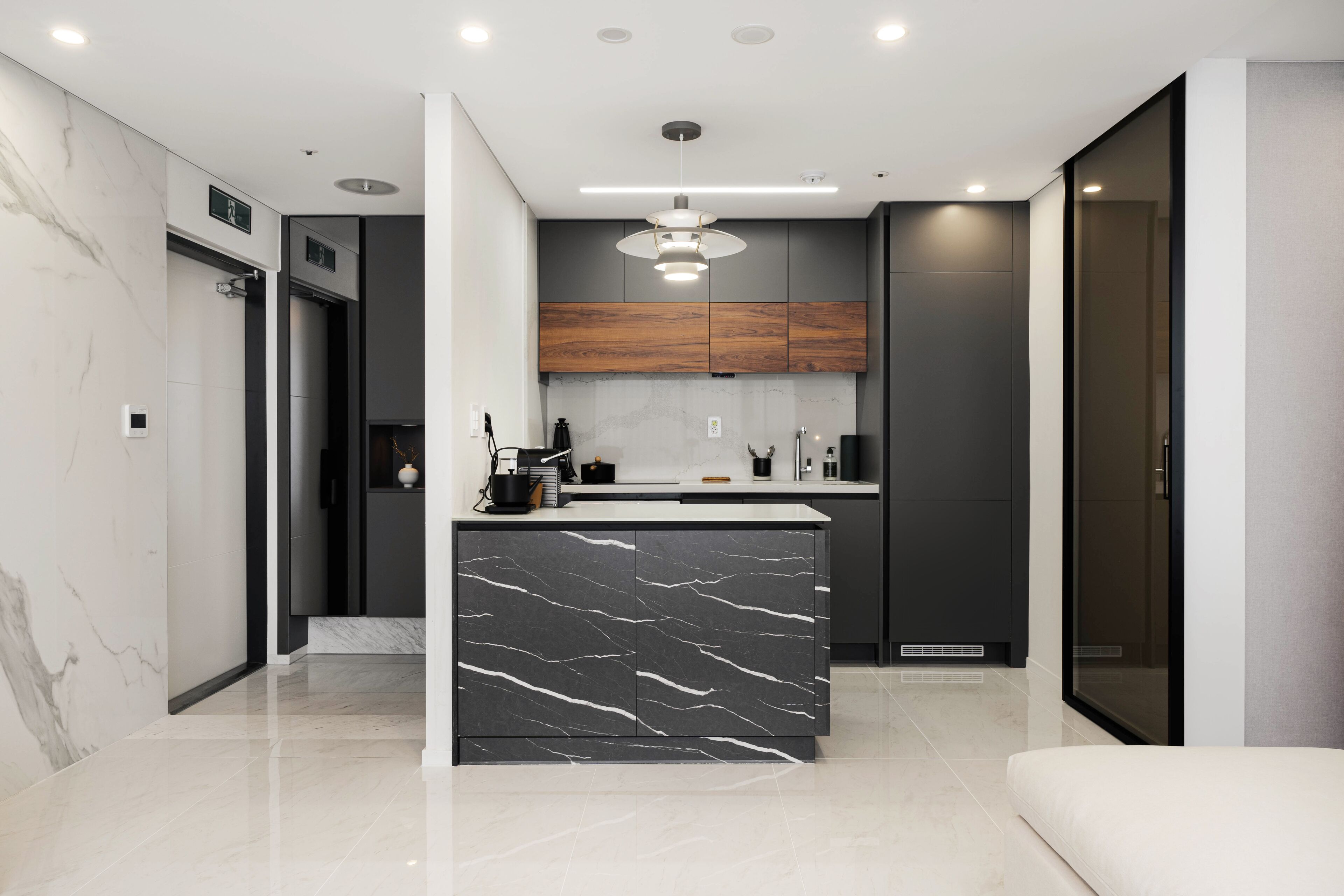 A modern kitchen with a marble island, dark cabinets, and a pendant light.