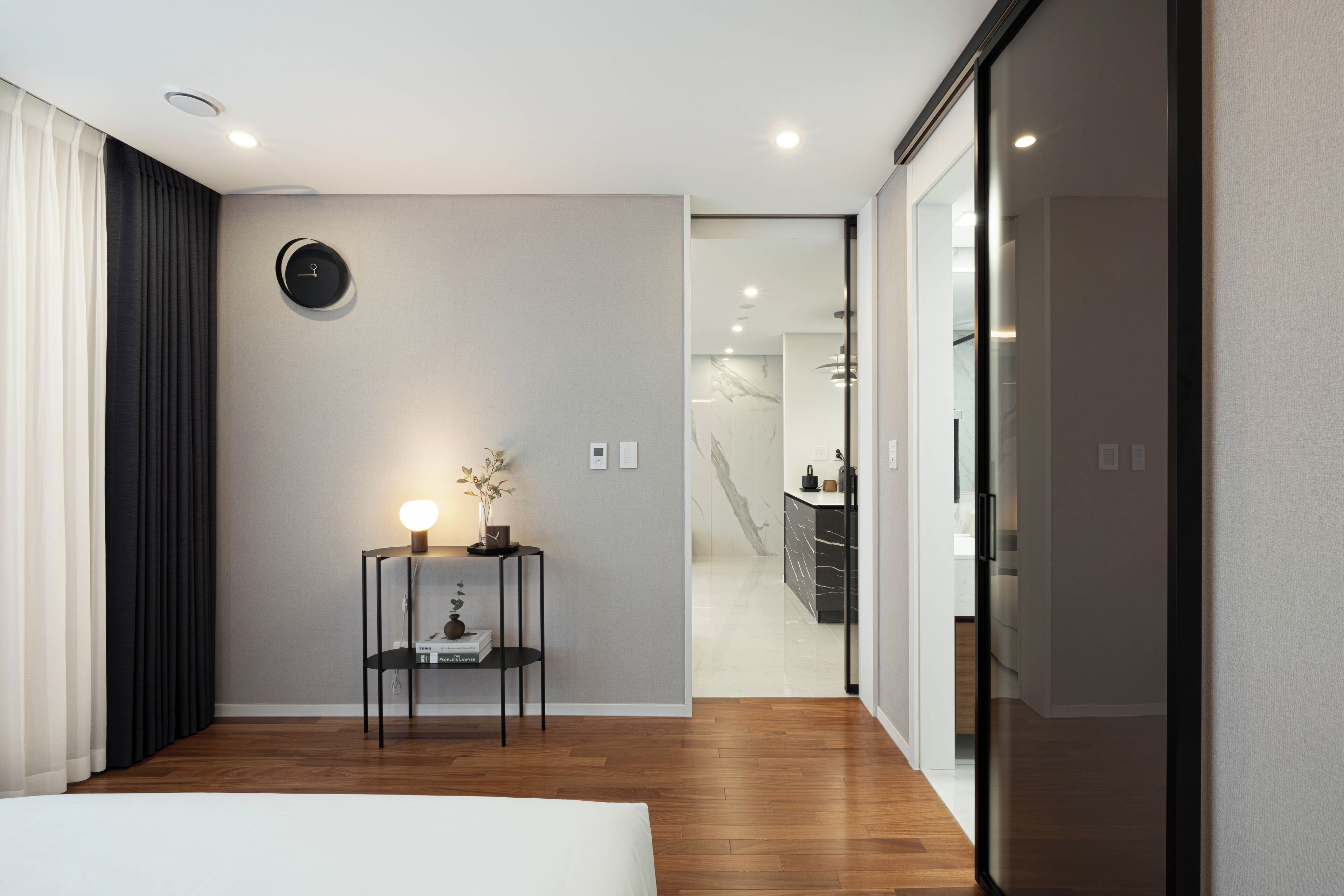 Un dormitorio moderno con suelo de madera, una mesita de noche con lámpara y vistas al baño.