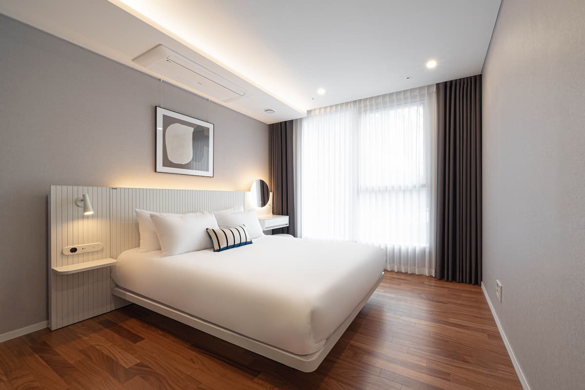 A modern hotel room with a large bed, bedside tables, a bedside lamp, a framed picture on the wall, and a window with curtains.