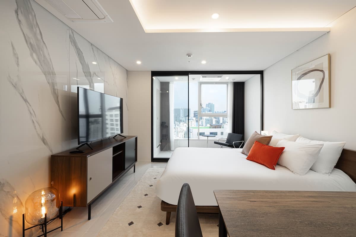 A modern hotel room with a large bed, a TV, a desk, and a city view.