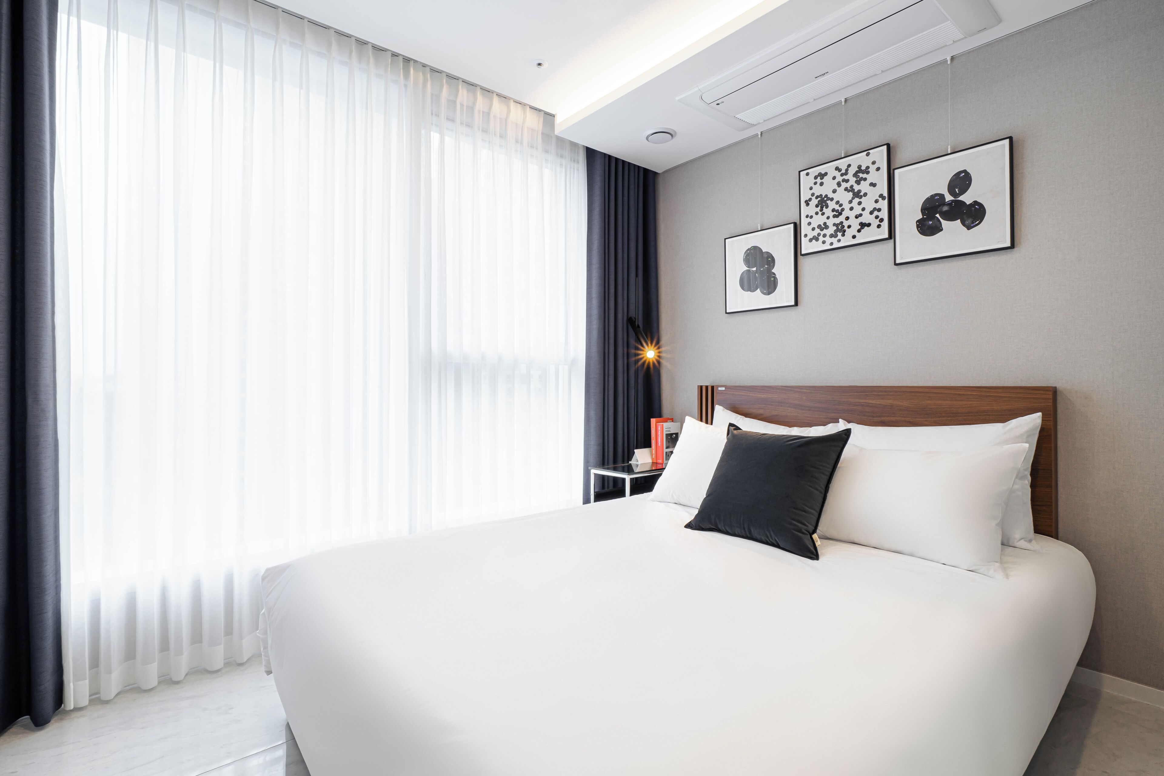 Une chambre d’hôtel moderne avec un grand lit, une table de chevet et une commode. Trois tableaux encadrés sont accrochés au mur au-dessus du lit.