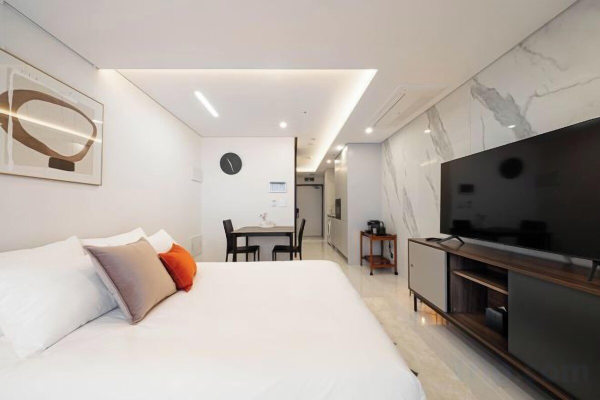 Habitación de hotel moderna con una cama grande, televisor, zona de comedor y pared de mármol.