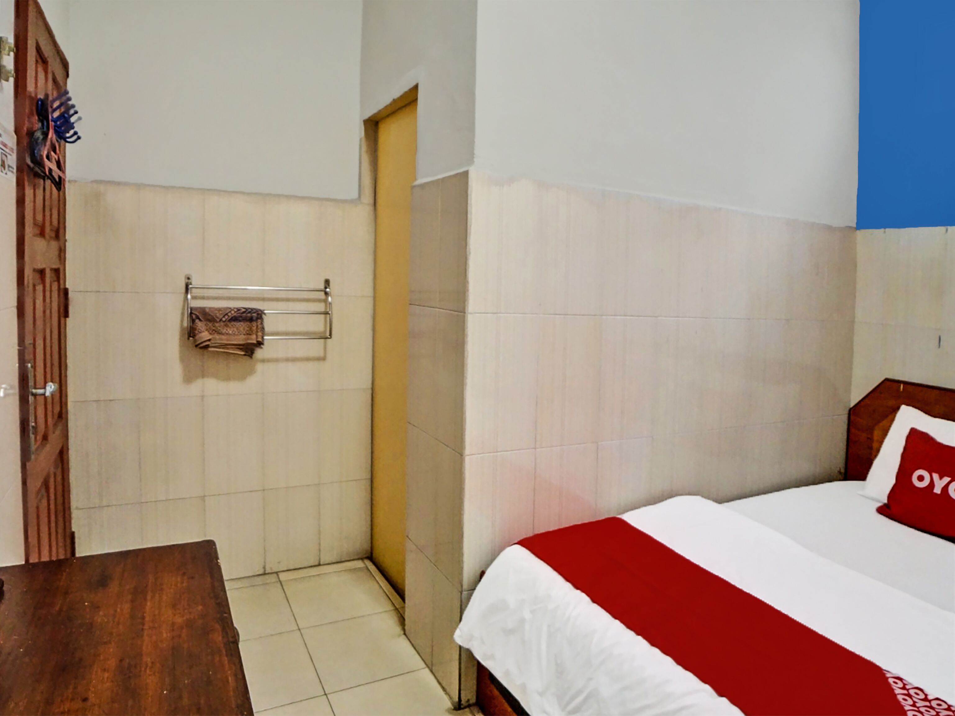 A hotel room with a bed, a wooden door, a towel rack, and a tiled floor.