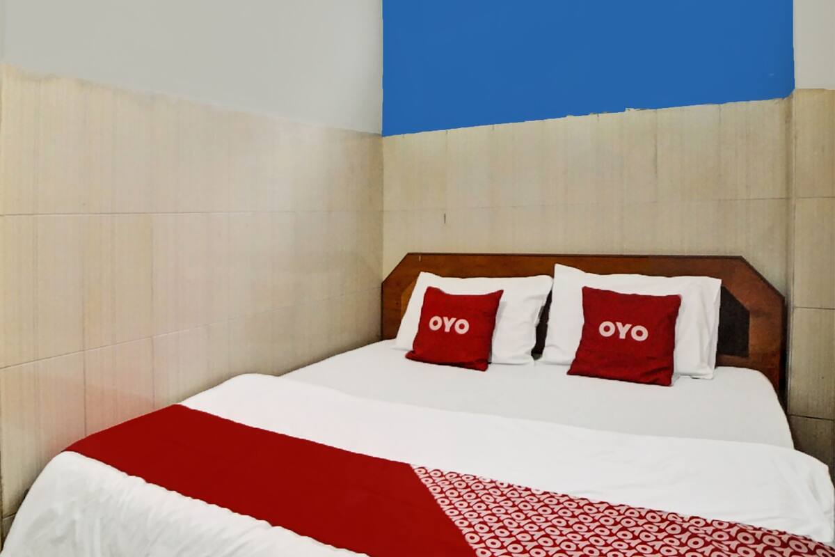 Hotellihuone, jossa on sänky, kaksi «OYO»-logolla varustettua tyynyä, punavalkoinen päiväpeite ja sininen seinä.