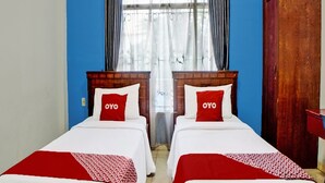A room with two beds, each with a wooden headboard and a red and white bedspread. There is a window with curtains and a view of the outside. - Hotel O Serena Anggrek (Medan)