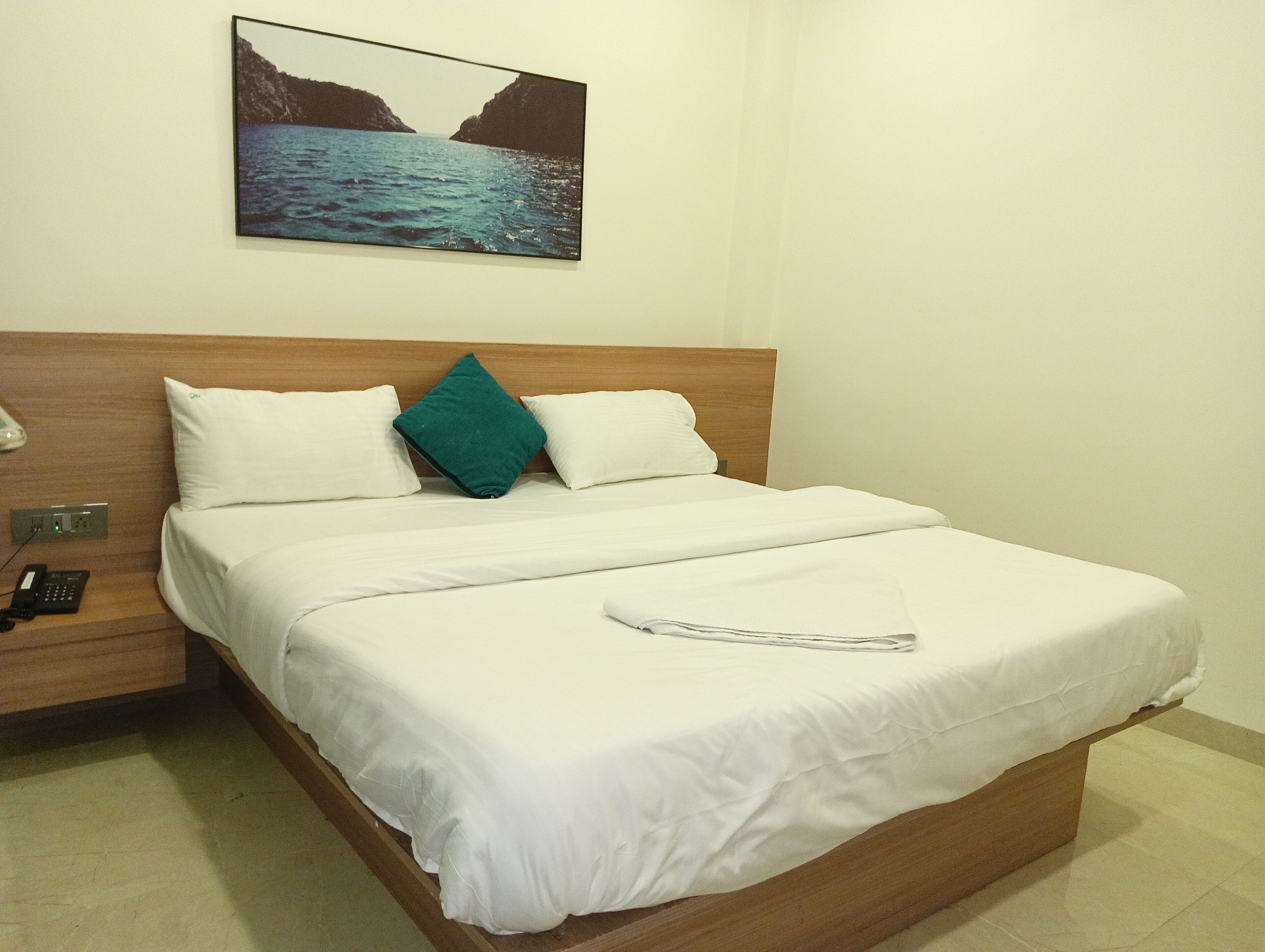 Una habitación de hotel con una cama, una mesita de noche con teléfono y un cuadro de un paisaje costero en la pared.