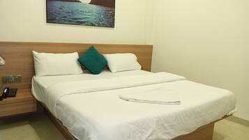 Una habitación de hotel con una cama, una mesita de noche con teléfono y un cuadro de un paisaje costero en la pared.