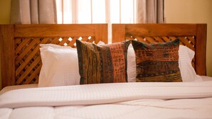 A bed with a wooden headboard, white bedding, and patterned pillows. - HECASA HOMESTAY (Arusha)