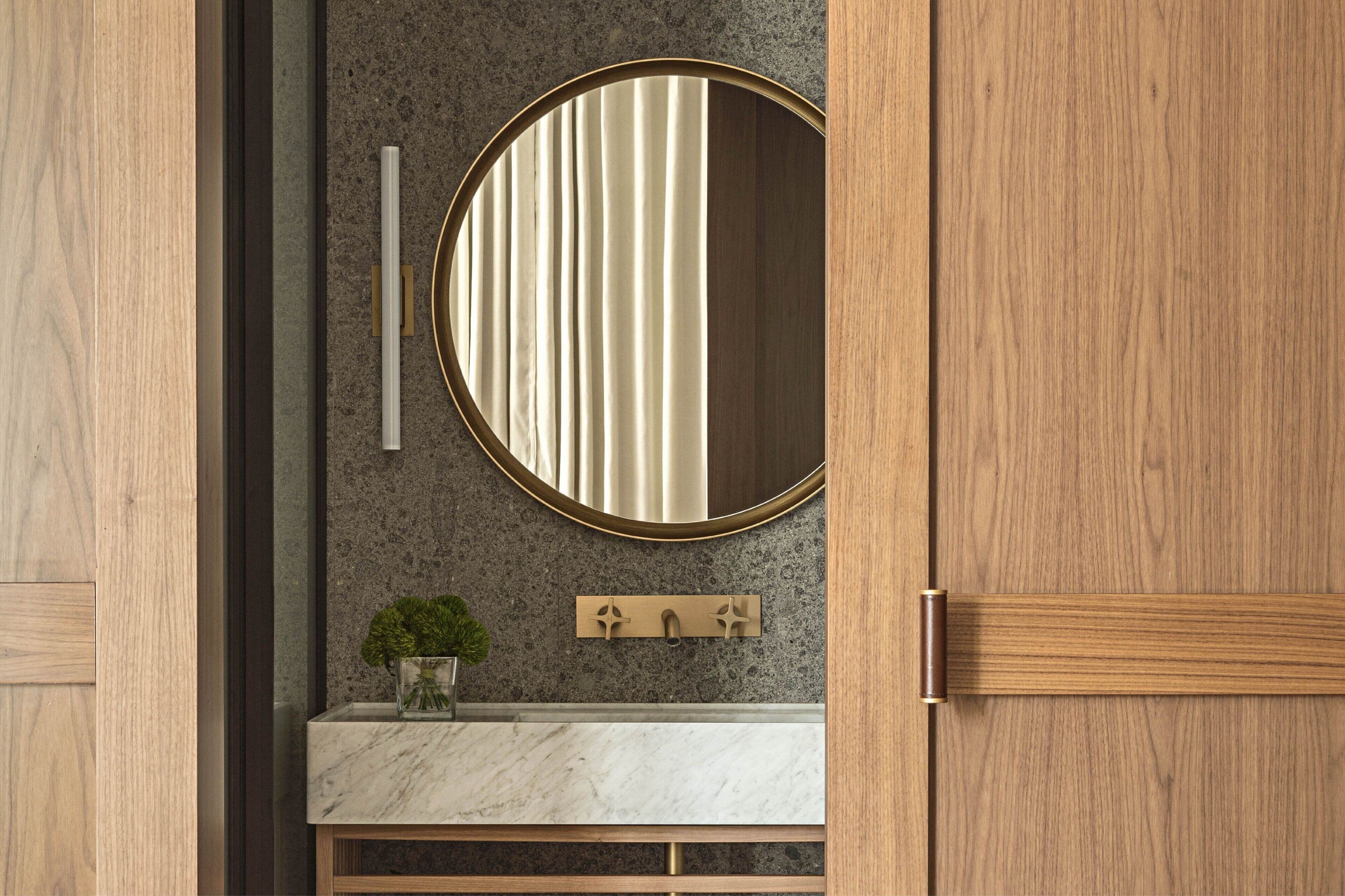 A bathroom with a wooden vanity, a round mirror, and a marble countertop.