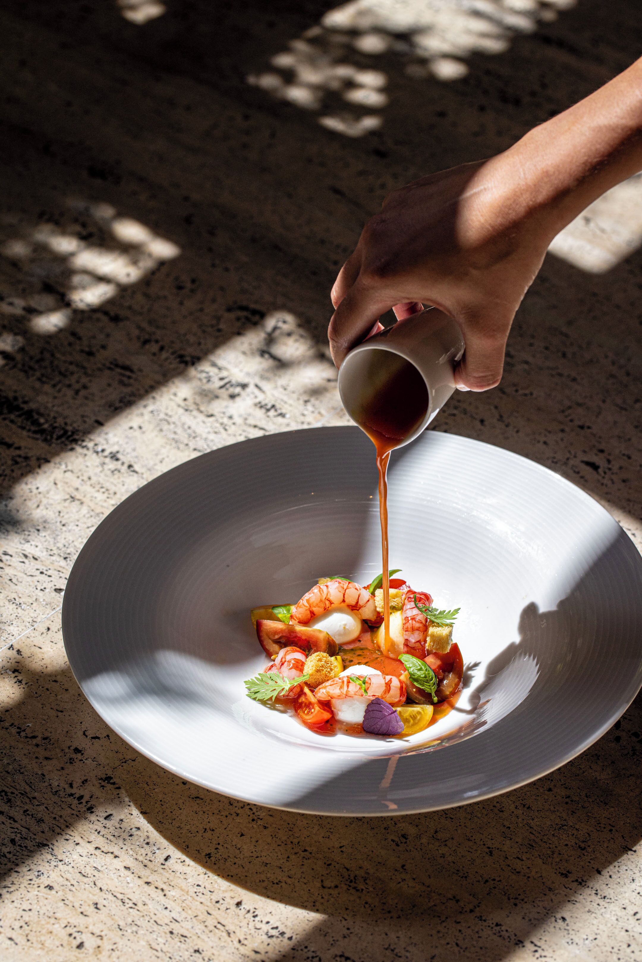 A hand pouring sauce over a dish on a plate.